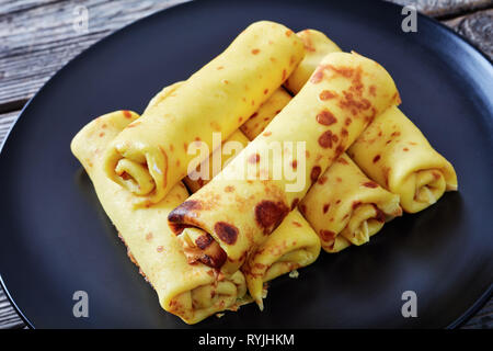 Close-up of Roll-Ups crêpe au fromage à la crème garniture sur une plaque noire sur une vieille table en bois, vue du dessus Banque D'Images