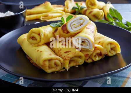 Close-up of Roll-Ups crêpe au mascarpone garniture sur une plaque noire sur une vieille table en bois avec feuilles de menthe fraîche et d'ingrédients à l'arrière-plan, v Banque D'Images