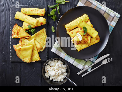 Roll Up crêpe au mascarpone garniture sur une plaque noire sur une vieille table en bois avec feuilles de menthe fraîche et d'ingrédients à l'arrière-plan, vue d'abo Banque D'Images