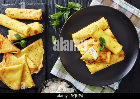 Roll Up crêpe au mascarpone garniture sur une plaque noire sur une vieille table en bois avec feuilles de menthe fraîche et d'ingrédients à l'arrière-plan, vue d'abo Banque D'Images