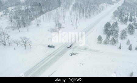 Quelques voitures qui passent à travers la couche de neige sur la route sur une vue aérienne avec les sapins couverts de neige pendant la saison d'hiver Banque D'Images