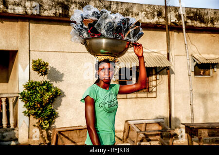 Sandales femme vendant ses marchandises transportant sur sa tête à Grand Bassam, Côte d'Ivoire. Banque D'Images