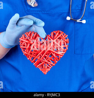 Médecin en uniforme bleu et des gants latex stériles est titulaire d'un gros cœur rouge, Close up Banque D'Images