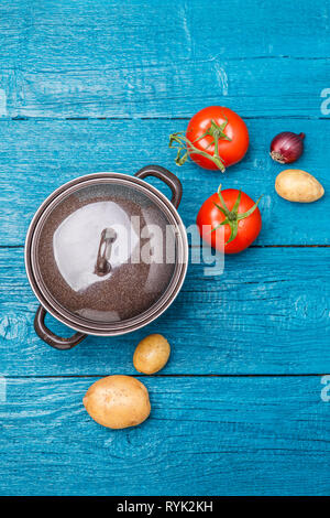 Image de pot de fer, tomate, pomme de terre, l'oignon sur fond en bois bleu. Banque D'Images