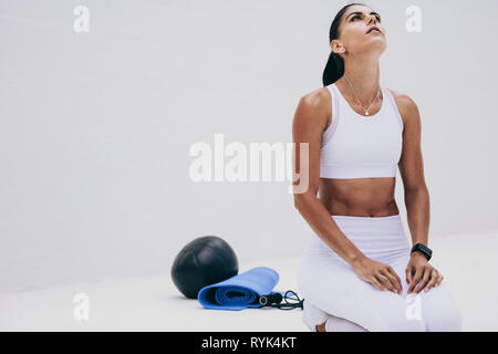 femme de fitness faisant de l'entraînement assis sur le sol regardant vers le haut. Femme faisant un entraînement de fitness avec son équipement de fitness à côté d'elle. Banque D'Images