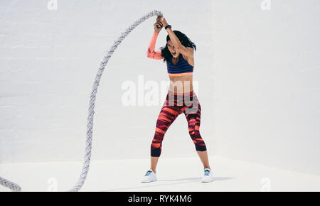 Femme en faisant porter à l'aide d'entraînement de remise en forme d'une bataille de la corde. Athletic woman lifting la bataille d'acier de haut en bas avec vigueur. Banque D'Images