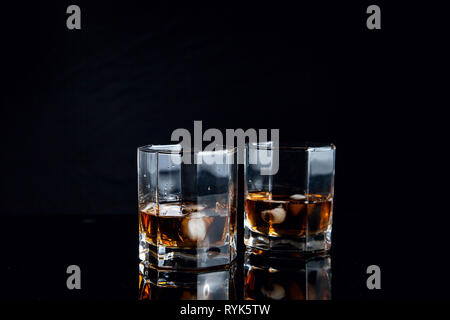 Les boissons alcoolisées et la conception. Deux verres de whisky avec des glaçons on reflective surface noire. Banque D'Images