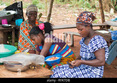 Akoupé, Côte d'ivoire-août 20, 2015 : trois jeunes femmes vendent de la nourriture , une femme est très occupé à hacher les oignons et les tomates à flovor vaisselle Banque D'Images