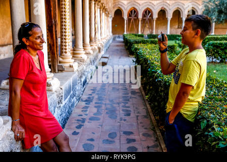 Jeune garçon de 12 ans de prendre une photo de sa mère dans le cloître de la cathédrale de Monreale, Sicile (Italie). Banque D'Images