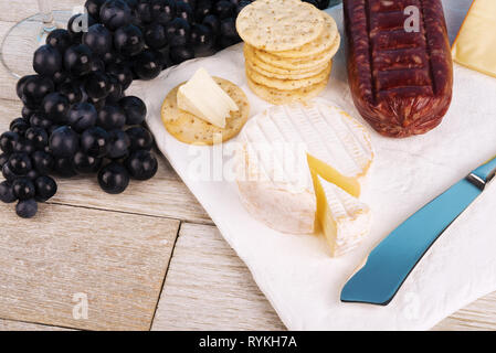 Le fromage, la charcuterie et les craquelins sur une plaque en céramique blanche. Planche en bois blanc en arrière-plan. Banque D'Images