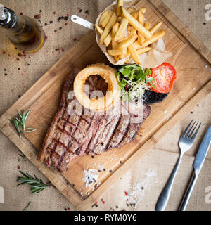 T Bone Steak de dessus avec chips, tomates et champignons sur une planche en bois et garnir avec de Hesse Banque D'Images