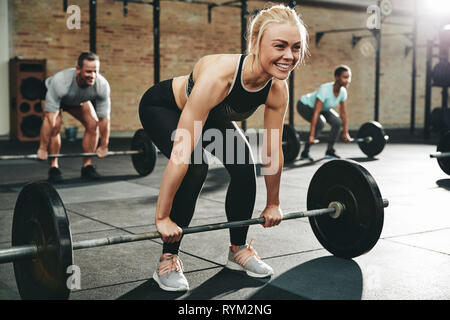 Fit young woman smiling in sportswear tout en se préparant à soulever des poids pendant une session au gymnase d'haltérophilie Banque D'Images