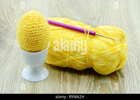 Les oeufs de pâques jaune crochet de laine à egg cup. la laine de ballons et crochet sur fond de bois. Banque D'Images