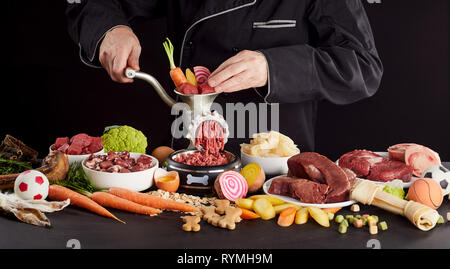 L'homme de la préparation des aliments sains pour son animal barf chien ou chat avec un assortiment de produits de viande et abats, légumes, céréales, d'œufs, d'oreilles de lapin, un os et chew Banque D'Images