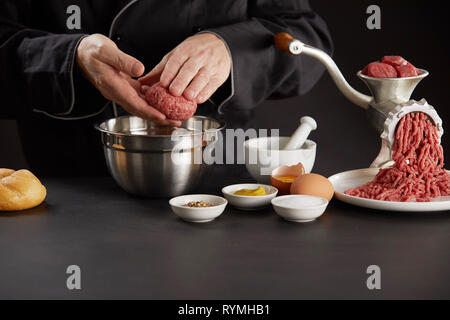 Man making boulettes de viande pour chien avec ses mains, la maintenant sur bol en métal. Ancien hachoir à viande manuel avec du bœuf haché sur table, et d'autres ingredi cuisson Banque D'Images