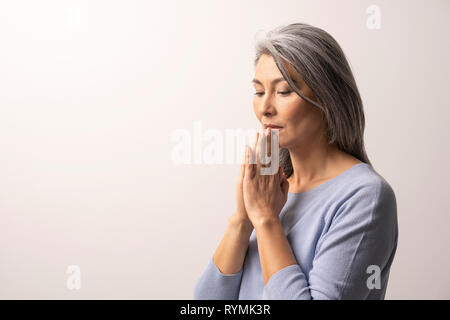 Mature Asian woman praying sur fond blanc Banque D'Images