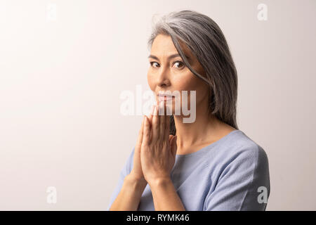 Mature Asian woman praying sur fond blanc Banque D'Images