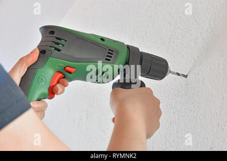 Les mains tenant un noir et vert de la machine de forage et de percer un trou dans un mur Banque D'Images