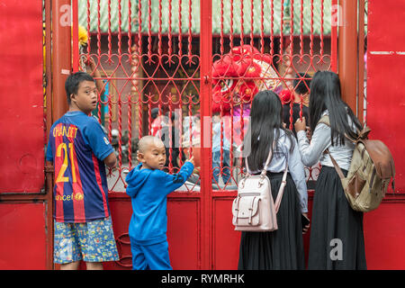 Stand des enfants le long d'une barrière métallique avec barres forgées peintes en rouge dont un garçon qui a les traits du visage d'une personne atteinte du syndrome de Down - Phnom Penh. Banque D'Images