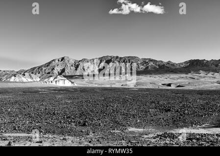 Les champs marqués d'un désert rocheux au-delà de montagnes arides, des nuages blancs moelleux. Noir et blanc. Banque D'Images