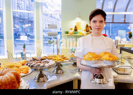 Jeune fille baker dans apron holding tray with pies dans une boulangerie Banque D'Images