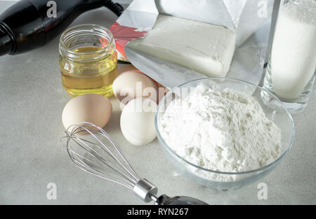 La farine et le sucre dans un récipient en verre, des œufs et du beurre sur un tableau blanc. Banque D'Images