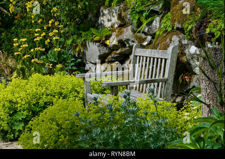 Jardin chaise au milieu de la floraison Alchemilla mollis et Baptisia australis, et d'autres plantes, adossé à la rock Banque D'Images