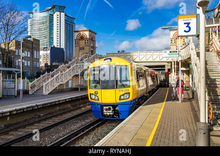 Un train terrestre de Londres en direction de Clapham Junction se dirige vers la gare de West Brompton avec l'Empress State Building au loin, Londres, Royaume-Uni Banque D'Images