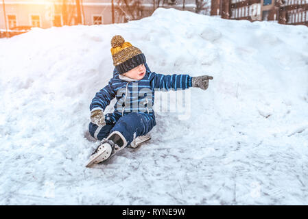 Un petit garçon de 3-5 ans, à l'hiver en extérieur dans un banc de neige et neige, reposant sur un week-end, assis dans une robe bleue et un chapeau chaud. Sur la neige Banque D'Images