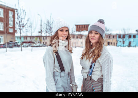 Deux jeunes filles amies en hiver dans la ville, se tenir en salopette dans pulls et accueil chaleureux des chapeaux, sur une patinoire de la ville. Happy smiling, détente à la Banque D'Images