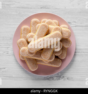 Savoyardi ou biscuits biscuits cookies sur la plaque en bois blanc, rose sur la surface, vue du dessus. Mise à plat, les frais généraux, d'en haut. Banque D'Images