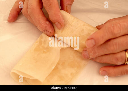 Les mains de la femme senior font des petites pâtisseries au fromage. Les mains du chef cuisent de près des feuilles de pâte feuilletée au fromage Banque D'Images
