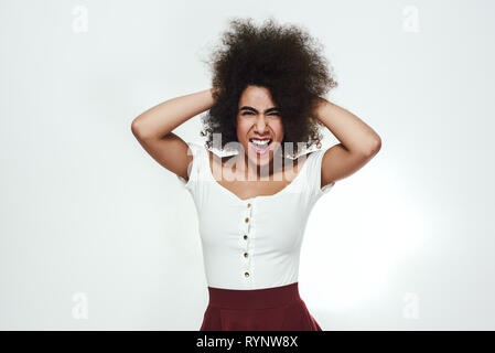 Devenir fou ! Ludique et femme excité lui touchant les cheveux bouclés, looking at camera, criant et en se tenant debout à l'arrière-plan gris. La beauté des femmes. L'humeur ludique Banque D'Images