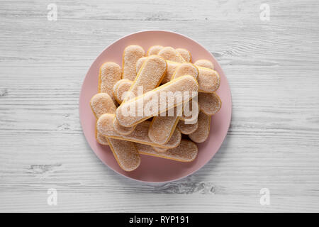 Savoyardi ou biscuits biscuits cookies sur la plaque rose sur fond de bois blanc, vue du dessus. Mise à plat, les frais généraux, d'en haut. Banque D'Images