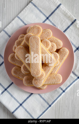Savoyardi les biscuits sur la plaque en bois blanc, rose sur la surface, vue du dessus. Mise à plat, les frais généraux, d'en haut. Banque D'Images