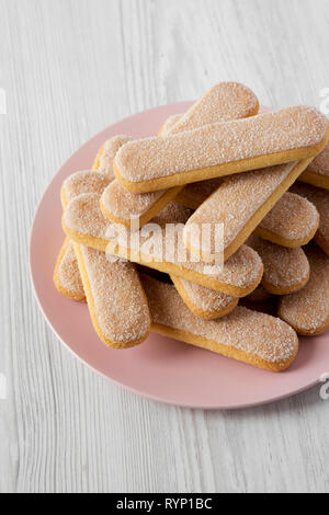 Savoyardi les biscuits sur la plaque rose sur fond de bois blanc, low angle view. Banque D'Images
