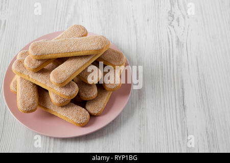 Savoyardi les biscuits sur la plaque en bois blanc, rose sur la surface, low angle view. Copier l'espace. Banque D'Images