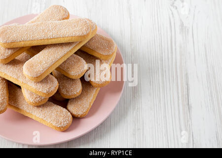 Savoyardi les biscuits sur la plaque rose sur fond de bois blanc, low angle view. Copier l'espace. Banque D'Images