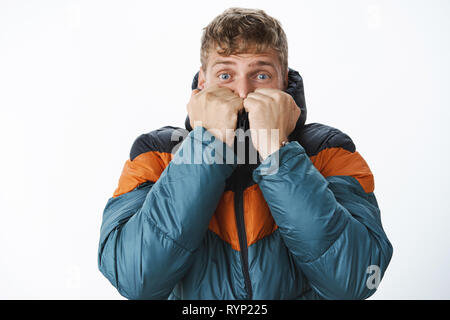 L'homme se cachant de l'hiver et la neige en tirant sur le col veste puffer visage sourcils sensibilisation et de grands yeux effrayés de temps froid, le réchauffement que l'achat Banque D'Images