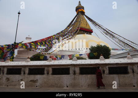 Un moine en passant par la filature et roues de prière à Boudhanath stupa sur un jour nuageux. Katmandou, Népal. Banque D'Images