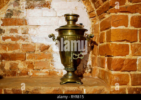 Samovar en cuivre antique se trouve dans la forme de décor sur le fond de la cheminée mur de brique rouge. Contexte, rétro, vintage. Banque D'Images