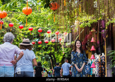 Hoi An, Vietnam - Octobre 23, 2018 : une jeune femme asiatique pose pour son ami (hors cadre) à côté de la promenade de deux femmes âgées voyageurs. Banque D'Images