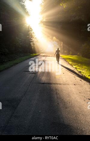 Jeune femme marche sur une rue, à la lumière du soleil qui brillait à travers les arbres, l'Oregon Coast Highway, Oregon, USA Banque D'Images