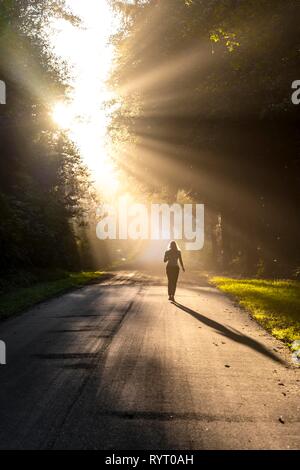 Jeune femme marche sur une rue, à la lumière du soleil qui brillait à travers les arbres, l'Oregon Coast Highway, Oregon, USA Banque D'Images