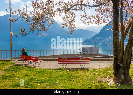 Girl enjoying vue sur la ville d'un banc sous le Magnolia arbre sur la colline à Lugano, vue sur le lac de Lugano et les montagnes des Alpes dans le canton du Tessin de SWI Banque D'Images