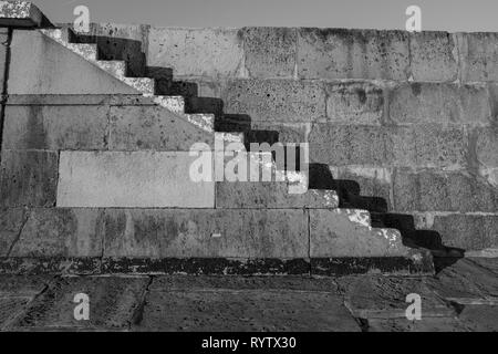 Vieux escaliers de pierre sur la Lyme Regis Cobb, tourné en noir et blanc avec des ombres contre le mur de pierre. Banque D'Images