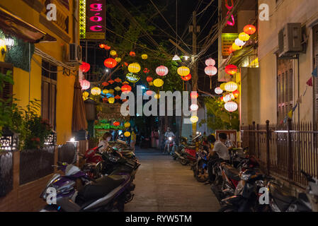 Hoi An, Vietnam - 13 novembre 2018 : une nuit backstreet décoré avec des lanternes de papier coloré avec des motos garées et plusieurs personnes. Banque D'Images