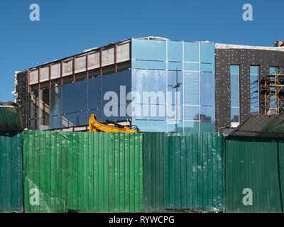 Clôture verte en face du site de construction. petit immeuble de bureaux ou de leur maison faite de verre, métal et béton Banque D'Images