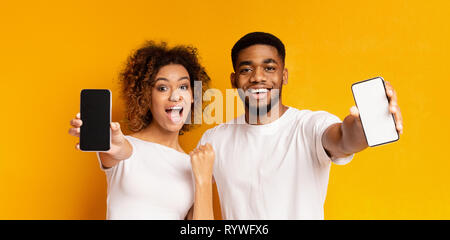 Cheerful black couple showing blank de smartphones Banque D'Images