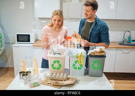 Le tri des déchets à la maison. Smiling young couple plaçant le plastique, papier, d'autres déchets dans des poubelles dans la cuisine bio Banque D'Images